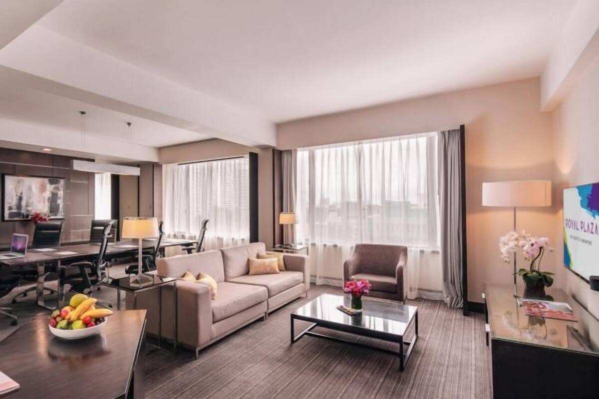 A modern hotel room with a sofa, armchair, coffee table, and a desk with a computer.