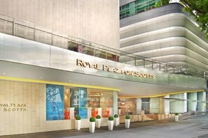 The exterior of Royal Plaza on Scotts, featuring a modern architectural design with a prominent glass facade and a series of white planters with green shrubs.