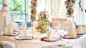 A wedding reception table set with white tablecloths, gold cutlery, and floral centerpieces.