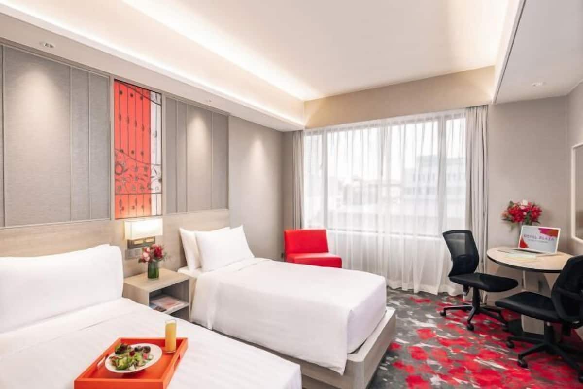 A hotel room with two beds, a desk, a chair, a small table, and a window with curtains.
