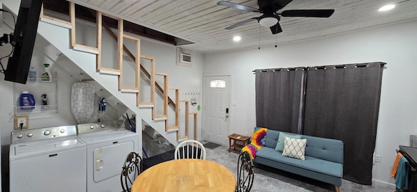 A compact living space with a kitchen, a dining area, a sofa, and a staircase.