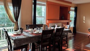 Uma área de jantar com uma mesa posta para quatro pessoas, cadeiras, uma janela com cortinas e vista para o verde lá fora.