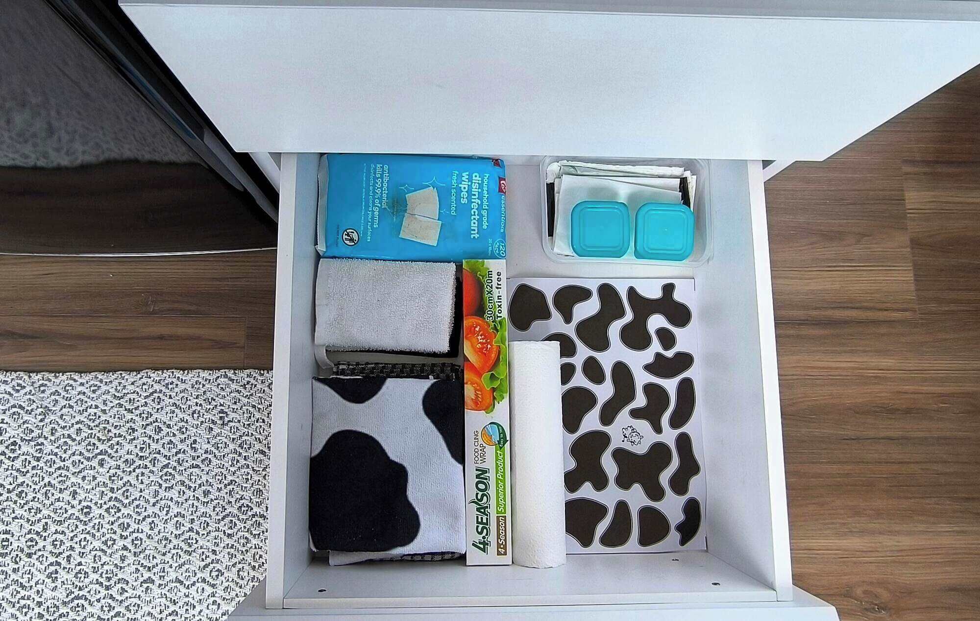 A drawer with various items including a blue box, a white towel, a black and white patterned cloth, and a roll of paper towels.
