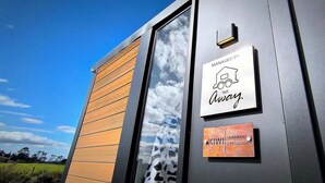 A building with a wooden panel facade, a sign indicating it is managed by 'Away', and a plaque for 'KIWI Taranaki Creekside'.