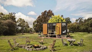 A modern, compact cabin with a wooden exterior, a deck, and a fire pit surrounded by outdoor seating.