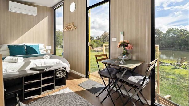 A bedroom with a bed, bedside tables, a desk, and a chair. There is a window with a view of greenery and a body of water.