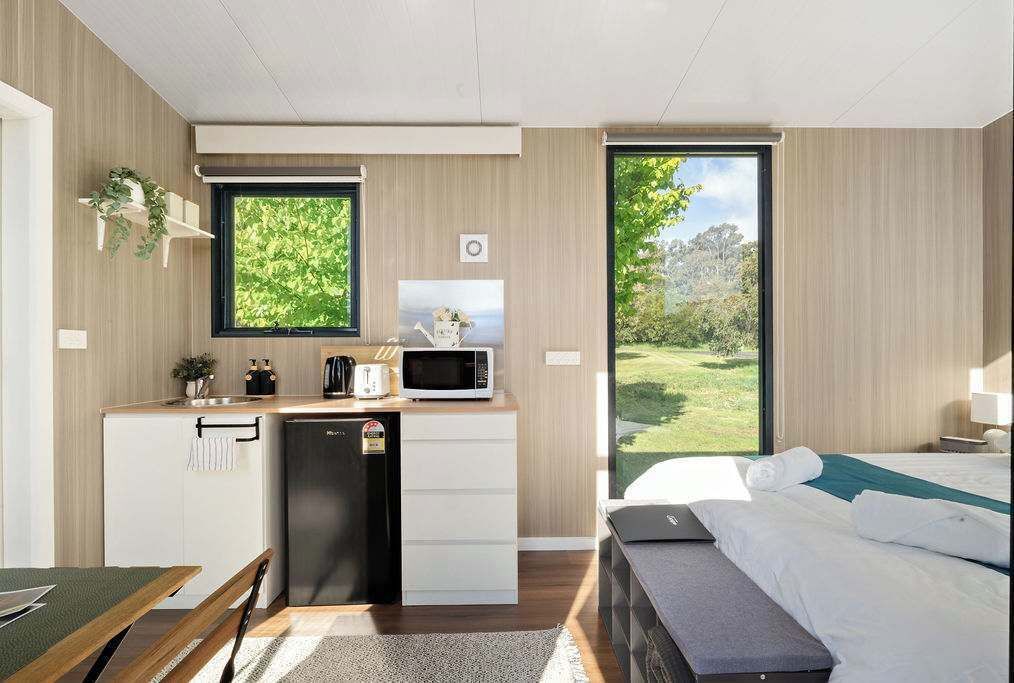 Ein kompaktes Hotelzimmer mit Küchenzeile, einem Bett und einem großen Fenster mit Blick auf Grünflächen.