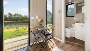 A modern room with a large window overlooking a lake, a wooden dining table with chairs, and a white bathroom with a mirror and sink.