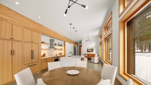 Een moderne keuken met houten kasten, een ronde eettafel en hangende lampen.