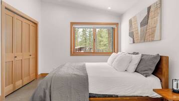 Un dormitorio con cama, ventana, armario y un cuadro en la pared.