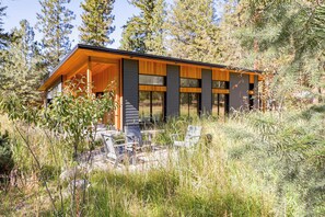 A modern cabin with a large deck, surrounded by tall grass and trees. - Gathering Pines – Trailside Modern 3BR in Mazama (Mazama)
