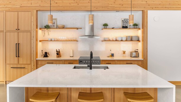 Een moderne keuken met houten kastjes, een groot kookeiland met krukken, hanglampen en een roestvrijstalen afzuigkap.