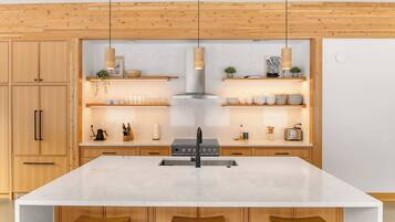 Una cocina moderna con armarios de madera, una isla grande con taburetes, iluminación colgante y una campana extractora de acero inoxidable.