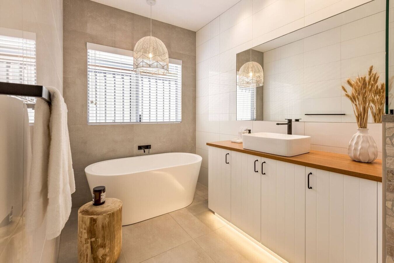 Een moderne badkamer met een vrijstaand bad, een grote spiegel en een houten wastafelmeubel.