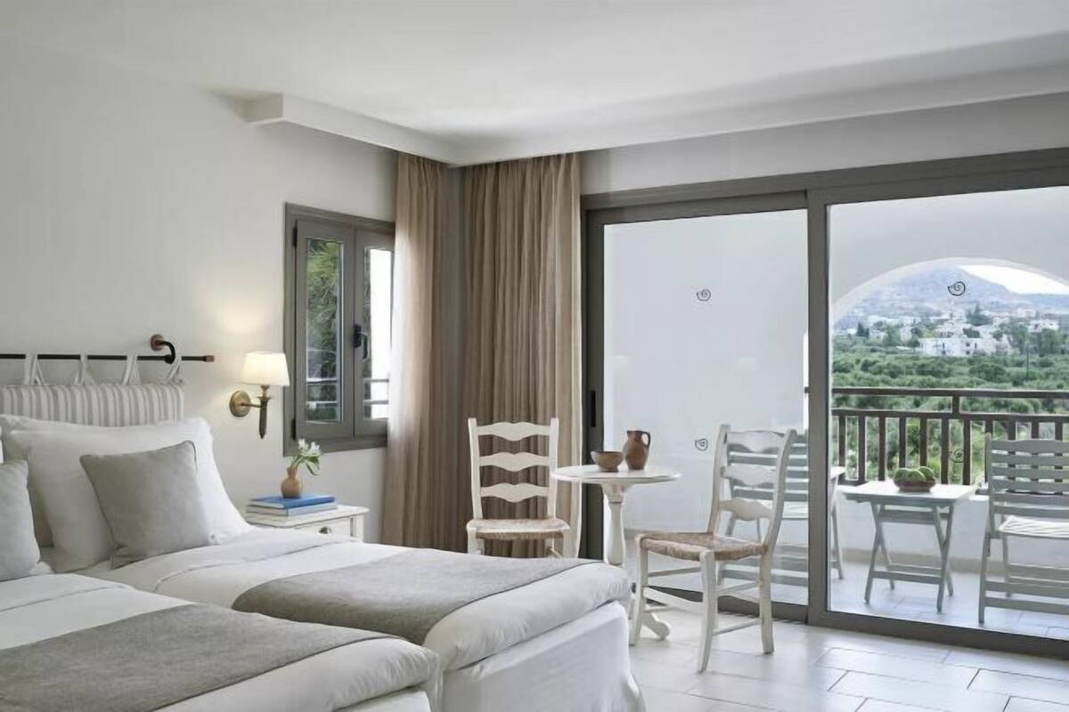 Une chambre d’hôtel comprenant un lit, un bureau, une chaise et un balcon avec vue sur une montagne et la verdure.