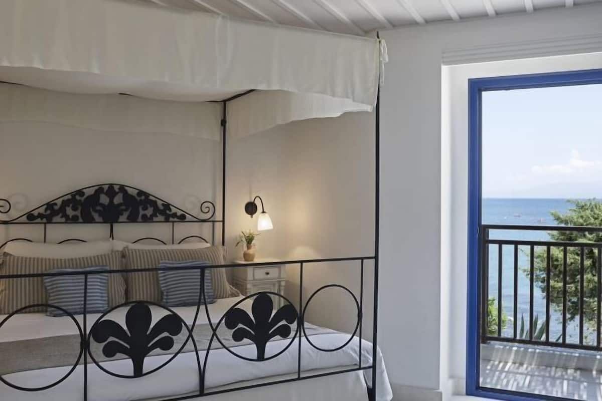 Une chambre à coucher avec un lit, une table de chevet, une lampe et une vue sur la mer depuis un balcon.