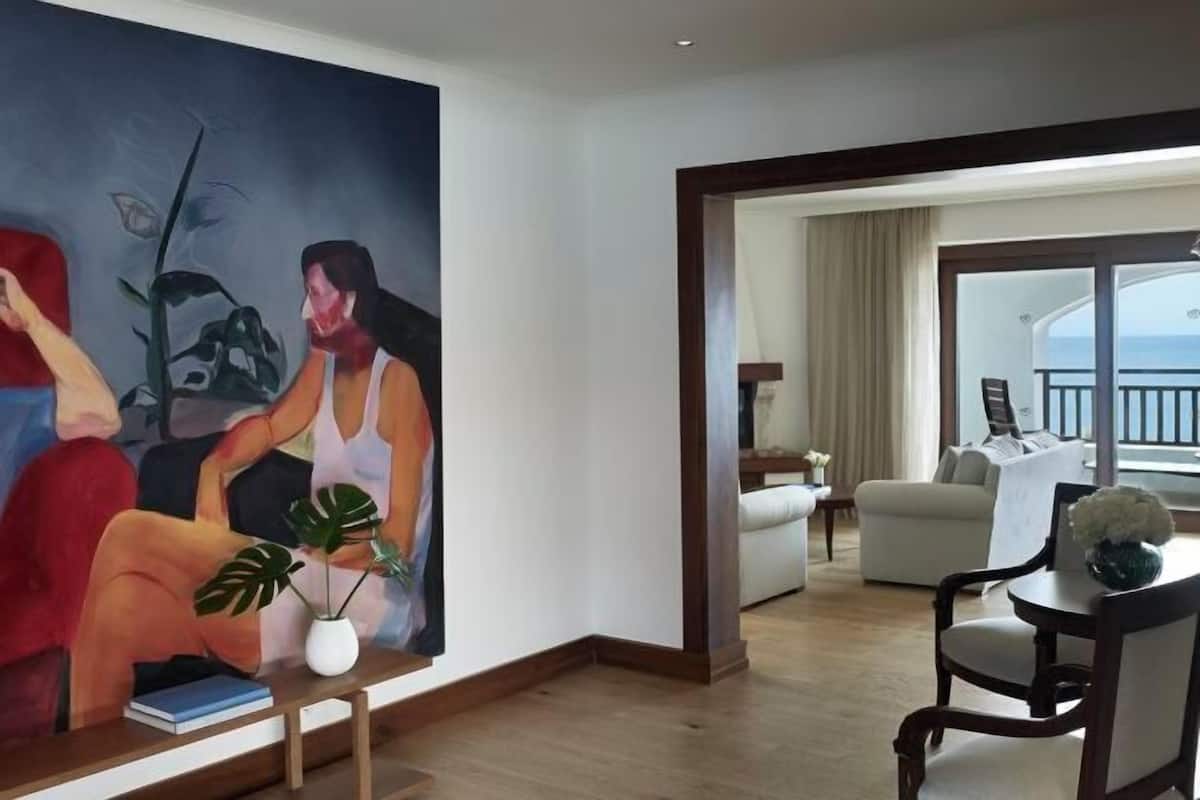 Un salon agrémenté d’un grand tableau, un coin repas avec une table et des chaises, et une vue sur la mer depuis un balcon.