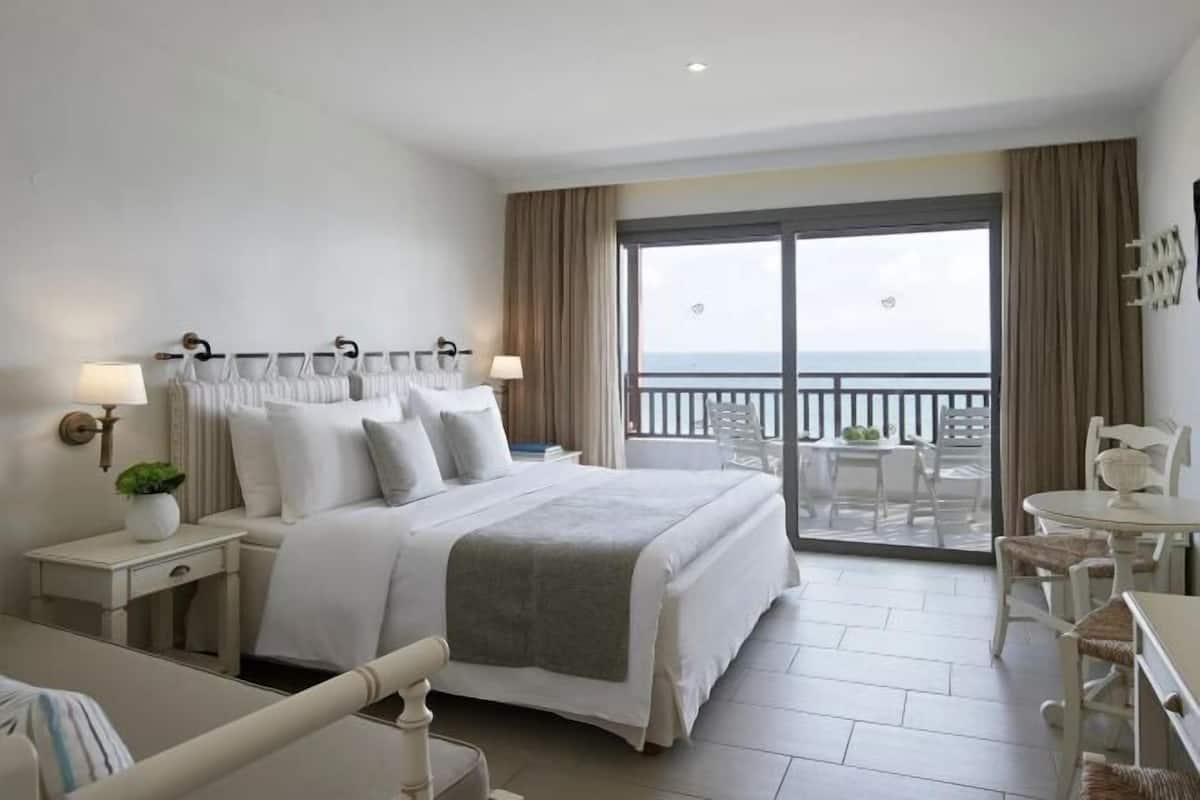 Une chambre d’hôtel comprenant un lit, des tables de chevet, un bureau, une chaise, un balcon avec vue et un coin repas.