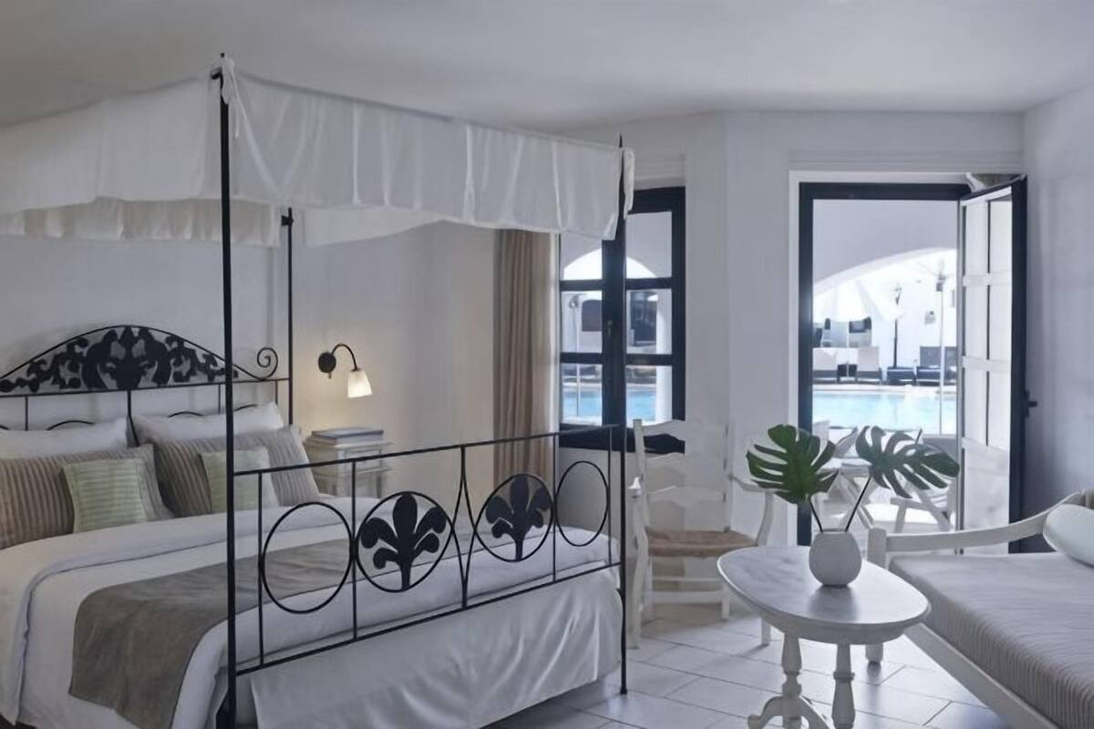 Un lit à baldaquin, une table de chevet avec une lampe, un canapé et une vue sur une piscine par une porte ouverte.