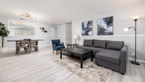 Un salon moderne avec un canapé gris, une table basse, un fauteuil bleu et un coin repas comprenant une table et des chaises.