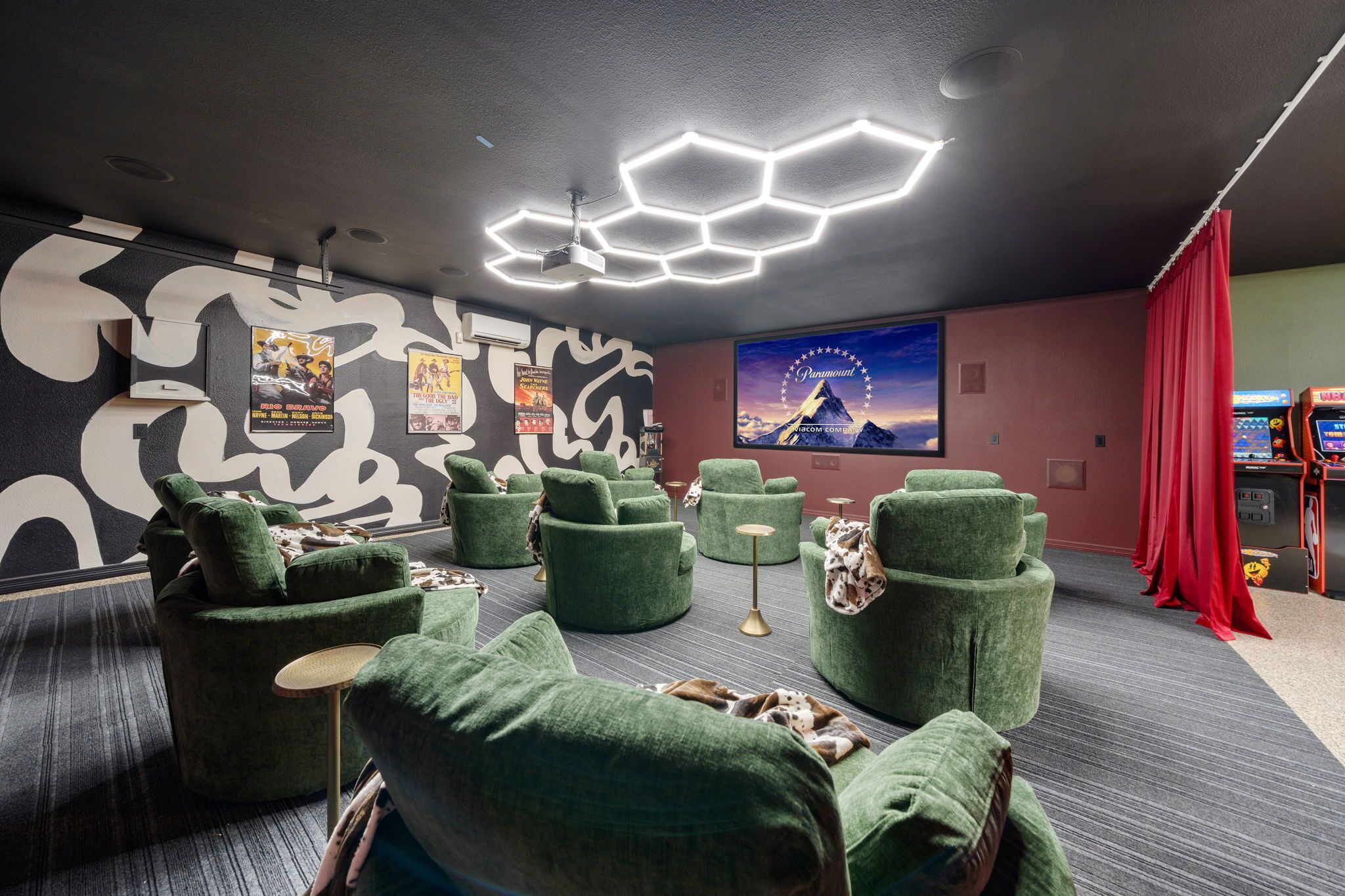 Ett modernt loungeområde med grönt klädda sittmöbler, hexagonformade taklampor och en stor affisch med ett bergslandskap.