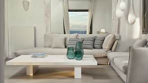 Un salon moderne avec un canapé blanc, une table basse blanche et une vue sur la mer par une fenêtre.
