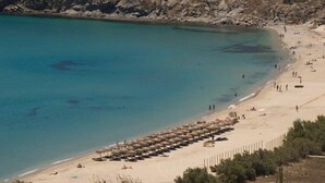 Une plage à l’eau turquoise et limpide, avec un rivage sablonneux et des parasols alignés le long de la plage.
