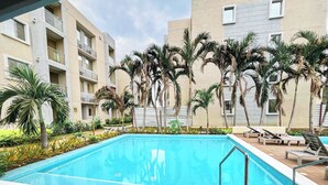 A swimming pool with lounge chairs and palm trees, surrounded by a building with balconies. - YOUR ESCAPE IN CARTAGENA! THE CARIBBEAN PARADISE! (Cartagena)