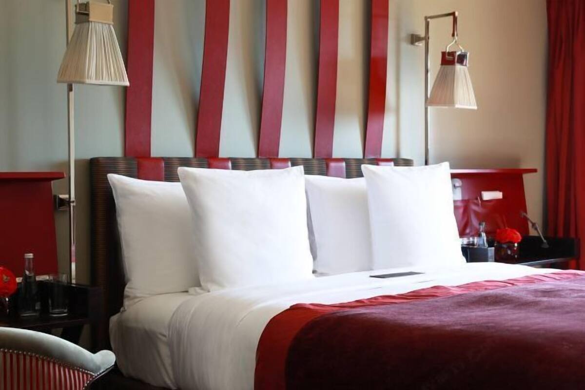 Una habitación de hotel con una cama, una mesita de noche, una lámpara y una cortina roja.
