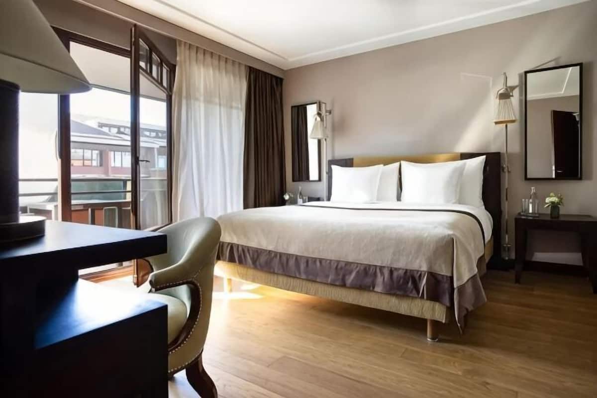 Una habitación de hotel con una cama, un escritorio, una silla, una mesita de noche y un ventanal con cortinas.