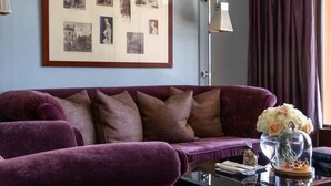 A purple sofa with a glass coffee table, a framed photo collage on the wall, and a window with curtains. - La Réserve Genève Hotel & Spa (Geneva)