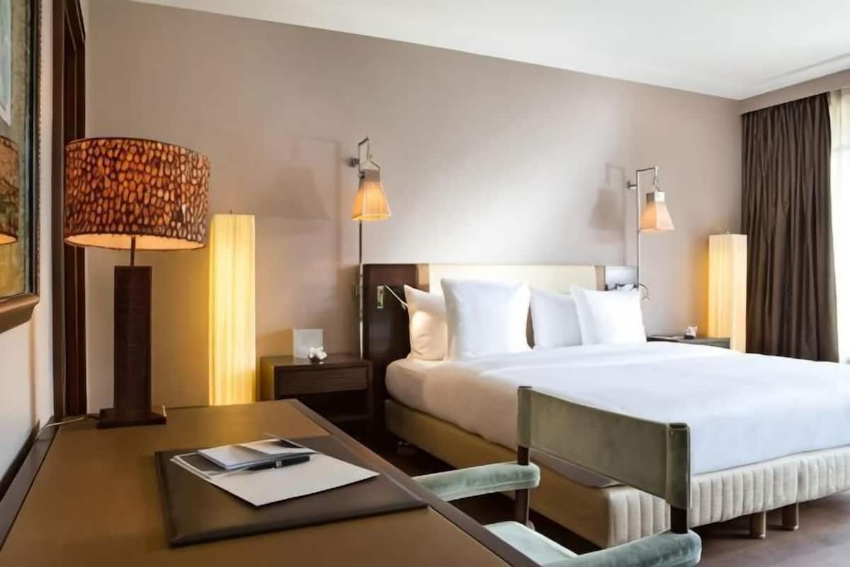 Habitación de hotel con cama, mesitas de noche, lámparas, escritorio y silla, y una ventana.