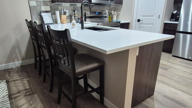 A modern kitchen with a central island, dark wooden chairs, a stainless steel refrigerator, and a microwave above the island. - Cozy Prairie (SUBDIVISION)