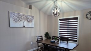 A dining area with a wooden table, two chairs, a bench, a chandelier, a wall-mounted clock, and a window with blinds. - Cozy Prairie (SUBDIVISION)