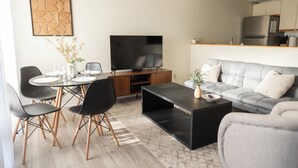 A modern living room with a dining area, a flat-screen TV, and a grey sofa. - 3-Bed Coastal Comfort in Biloxi (Gulfport)