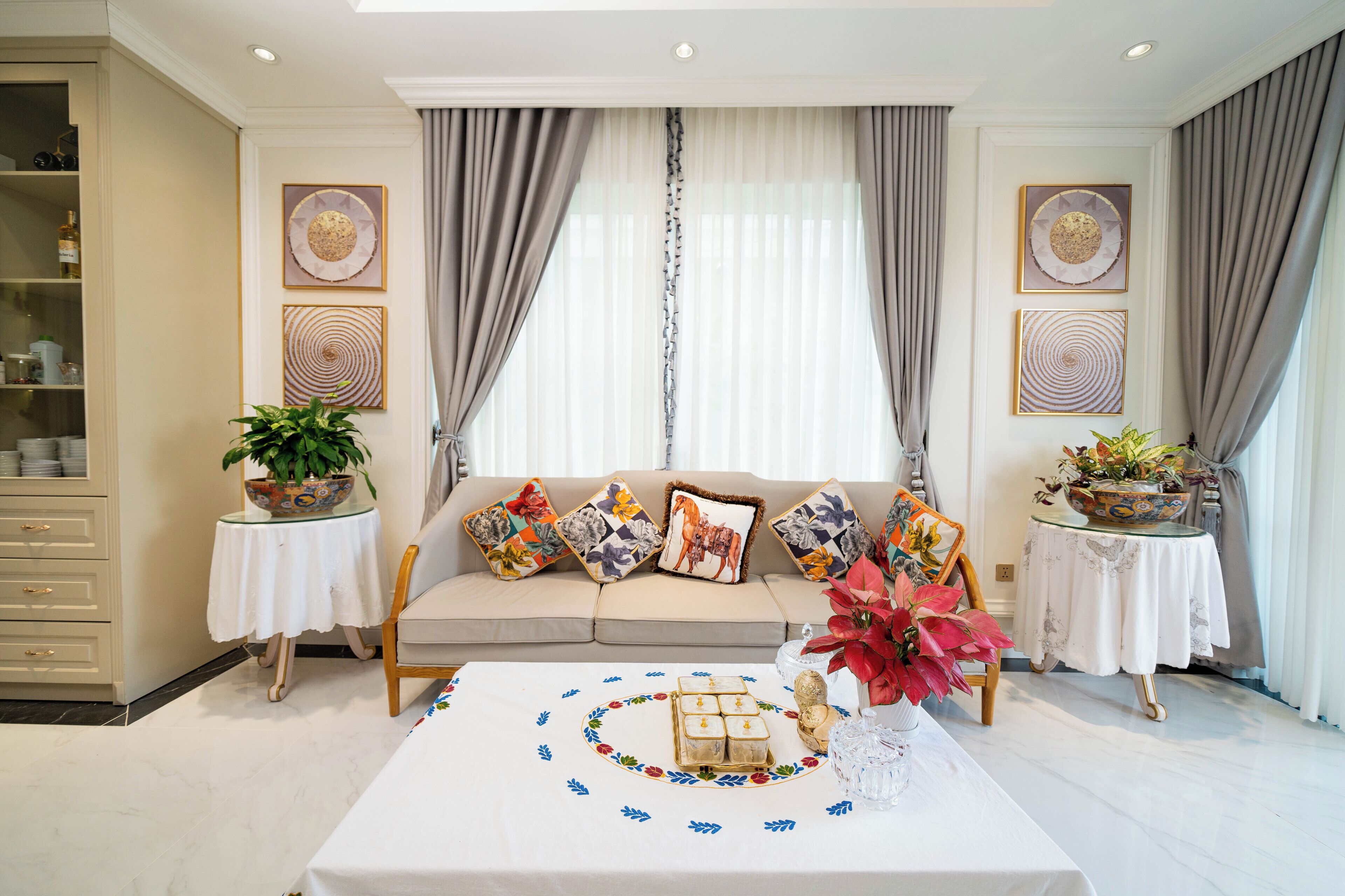 Un salón con un sofá, dos mesitas de noche con plantas, una mesa de centro con objetos decorativos y una estantería.