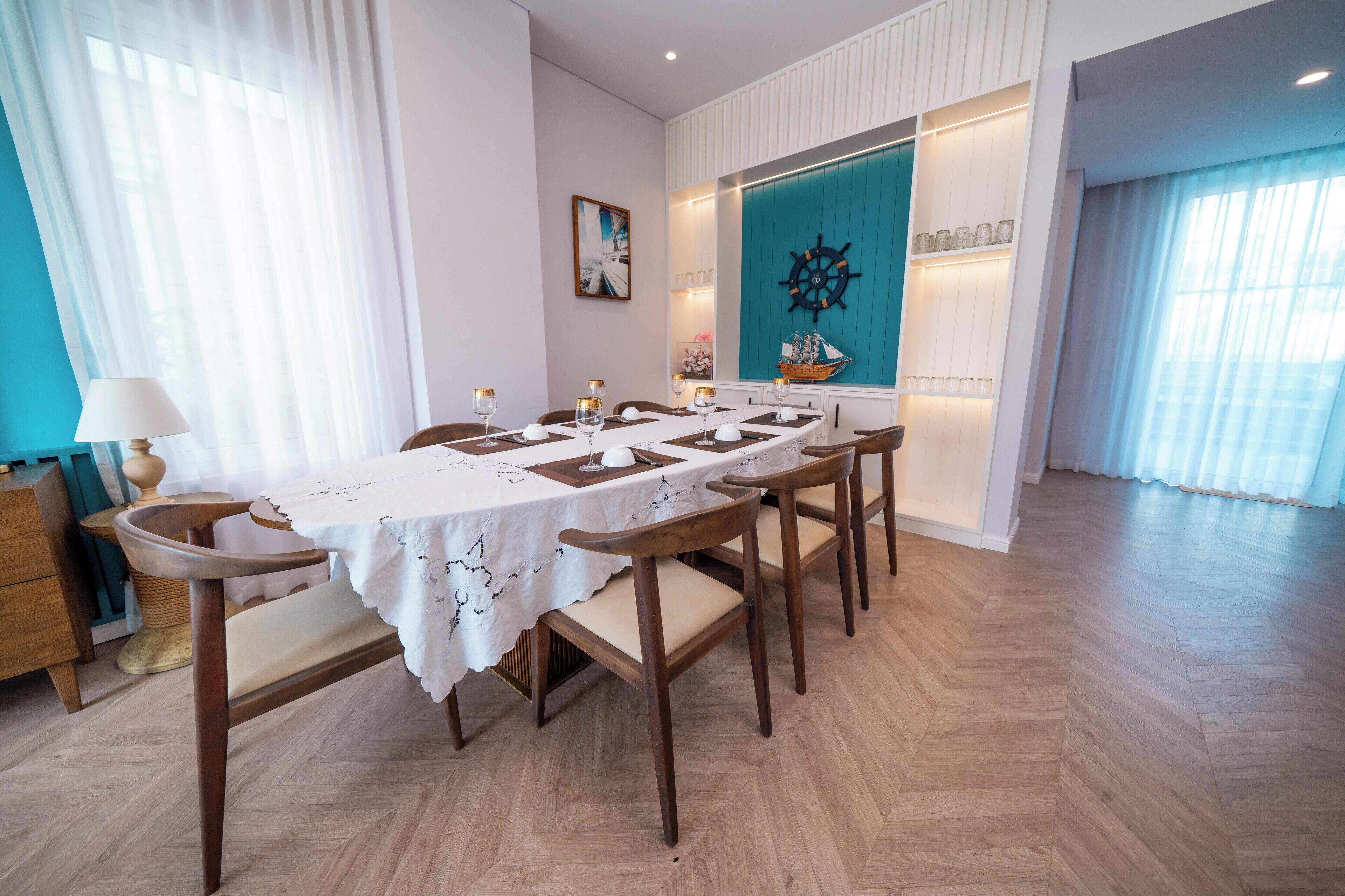 Een eetgedeelte met een lange tafel voor zes personen, houten stoelen, een decoratie in de vorm van een schipsschroef en uitzicht op de zee door grote ramen.