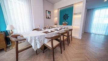Een eetgedeelte met een lange tafel voor zes personen, houten stoelen, een decoratie in de vorm van een schipsschroef en uitzicht op de zee door grote ramen.
