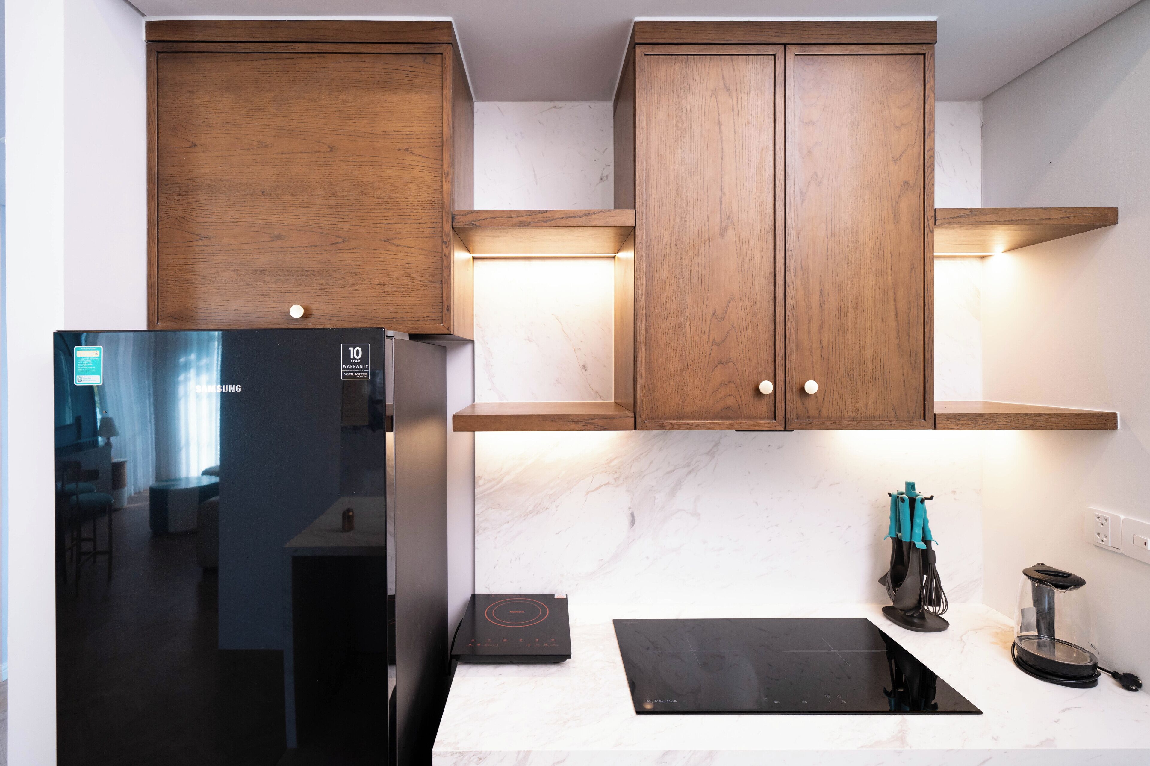 Eine moderne Küche mit Holzschränken, einem schwarzen Kühlschrank, einem eingebauten Induktionskochfeld und einer Glasabdeckung für Geräte.