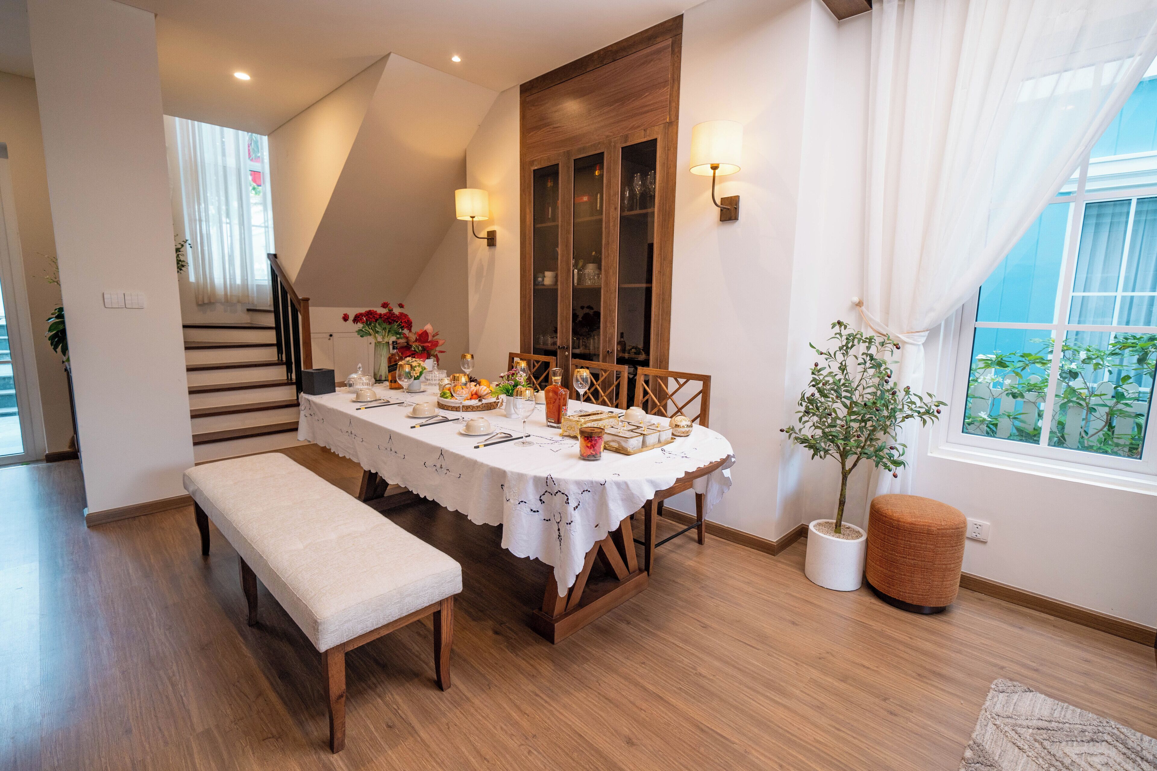 A dining area with a wooden table set for four, a bench, and a potted plant.