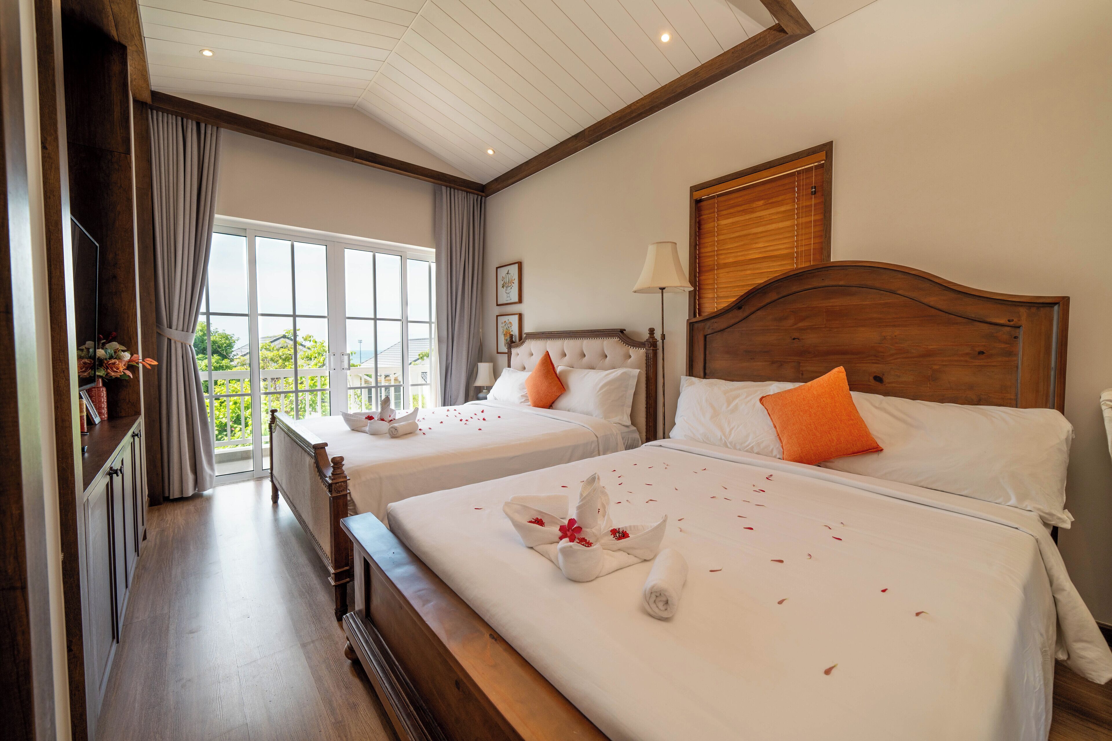 A hotel room with two beds, a large window, a wooden ceiling, and a view of greenery outside.