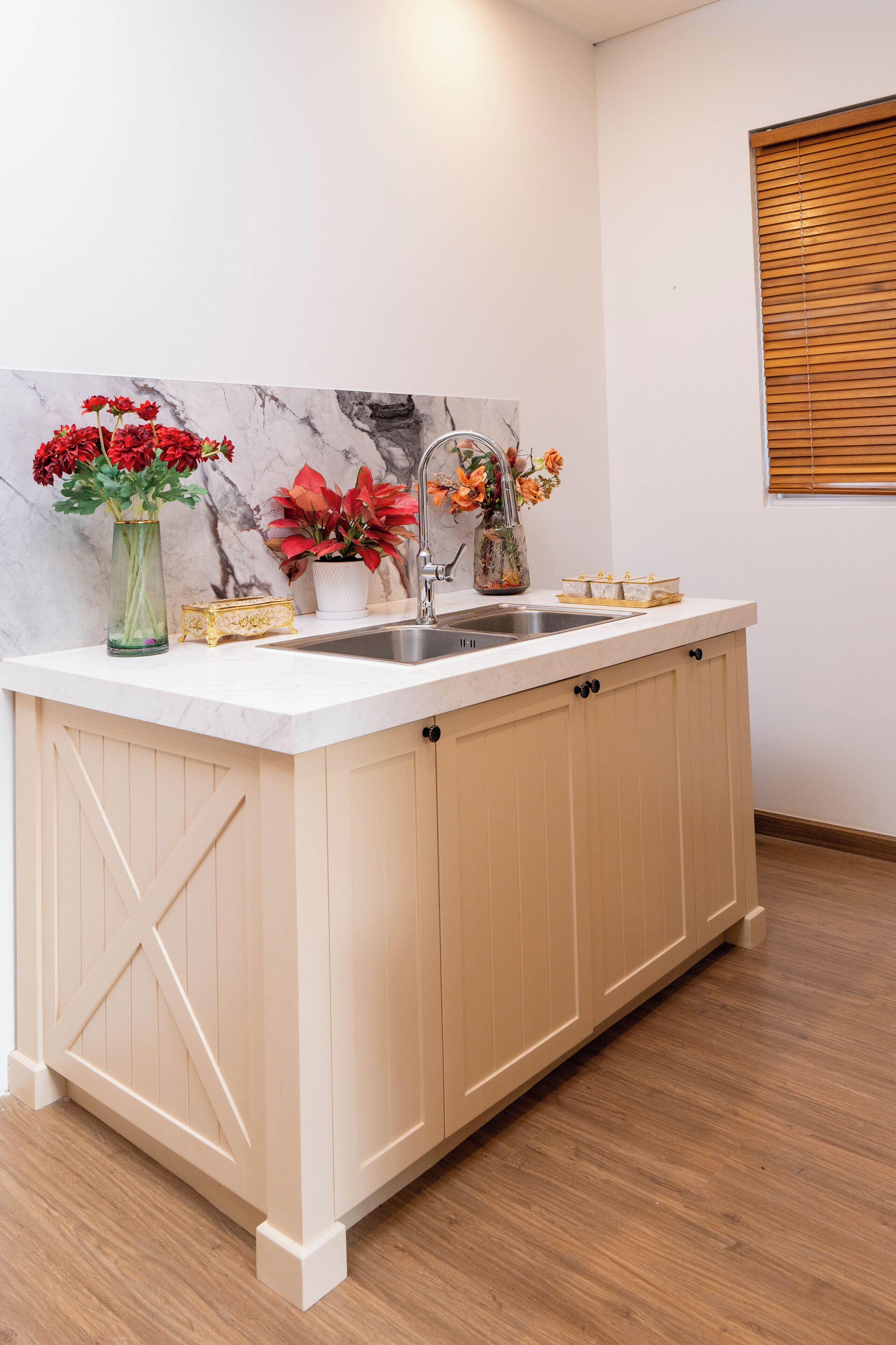 Une cuisine avec un plan de travail blanc, un évier et des placards en bois. On y trouve trois vases avec des fleurs sur le plan de travail.