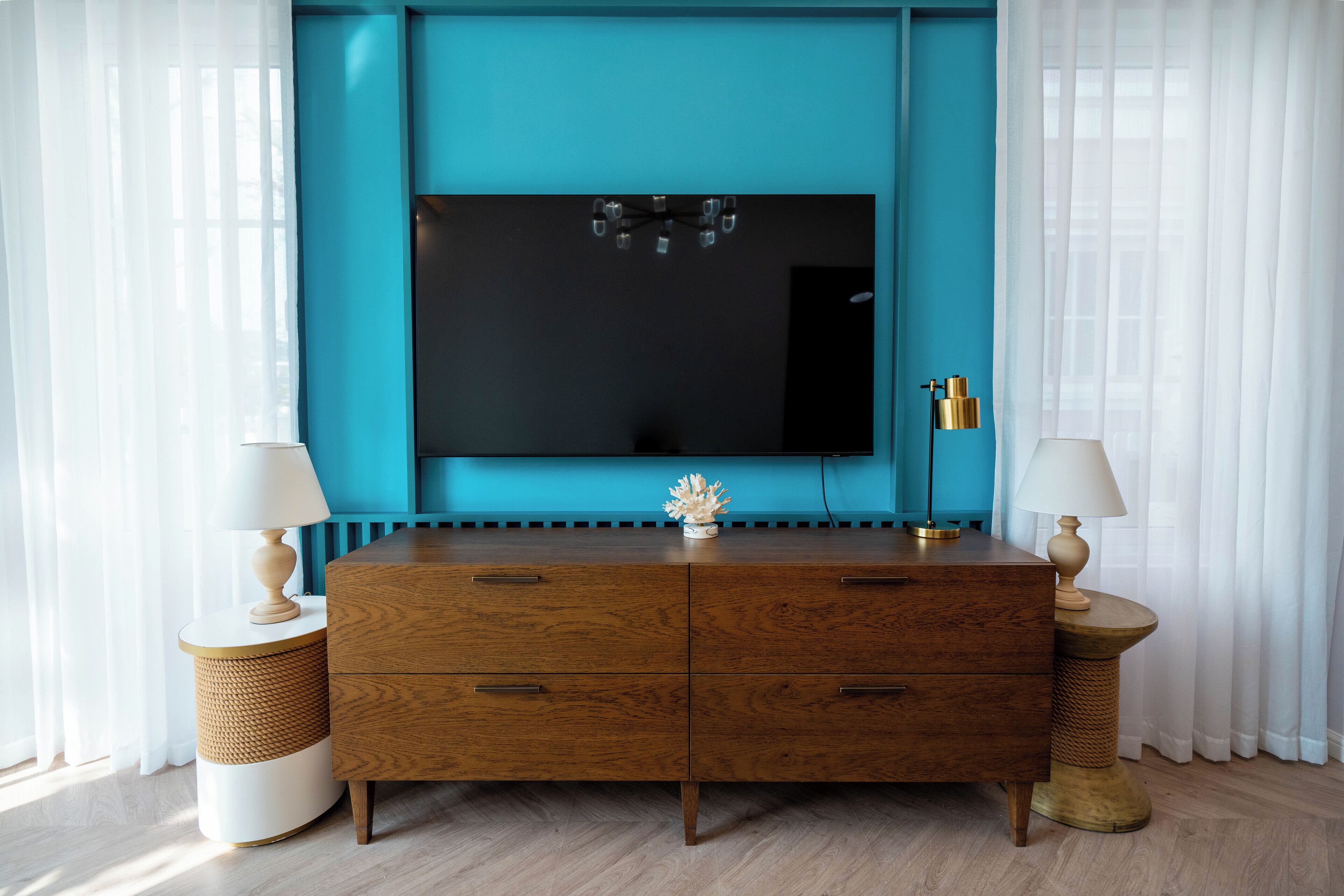 Un salon moderne avec un mur d’accent de couleur turquoise, un grand téléviseur à écran plat, des meubles en bois et deux tables d’appoint avec des lampes.