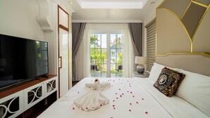A hotel room with a large flat-screen TV, a bed with rose petals, and a view of greenery through the window. - Chang Luxury Villa Beach View (Tien Thanh)