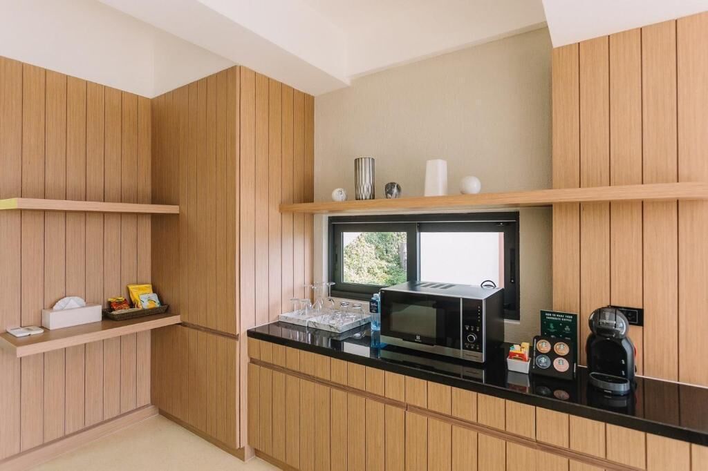 Une cuisine compacte dotée de meubles en bois, d’un plan de travail noir, d’un four à micro-ondes, d’une machine à café et d’une petite fenêtre qui laisse entrer la lumière naturelle.
