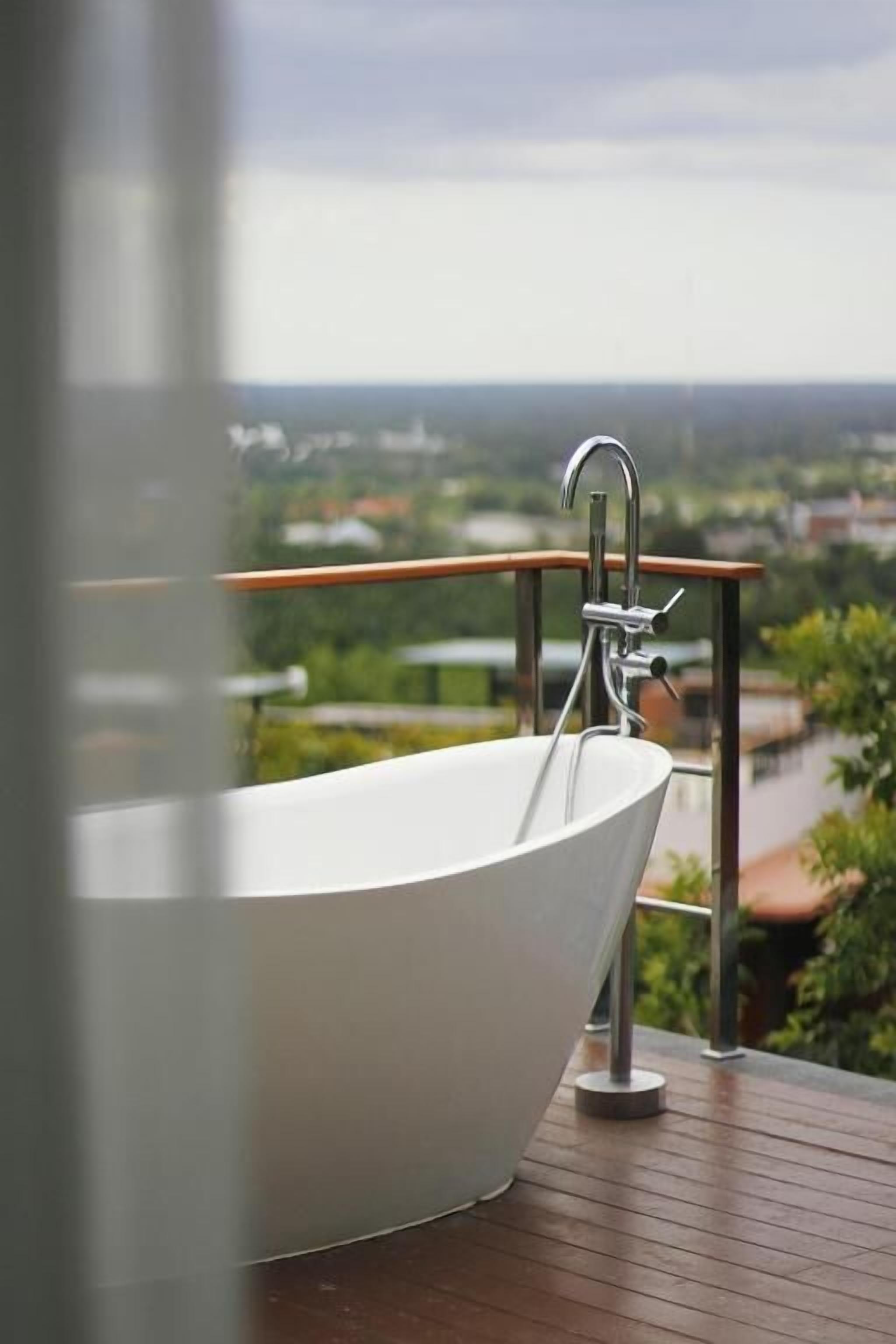 Un baño moderno con una bañera independiente sobre un piso de madera, con vistas a un río y edificios distantes.