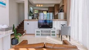 A modern living room with a TV, sofa, and kitchen area. - Sky Hill Villa Suratthani (Surat Thani)