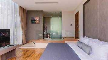 Quarto de hotel moderno com uma cama grande, uma televisão e uma porta de vidro para o banheiro.