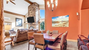 A dining area with a large table and chairs, a stone fireplace, and a television mounted on the wall.