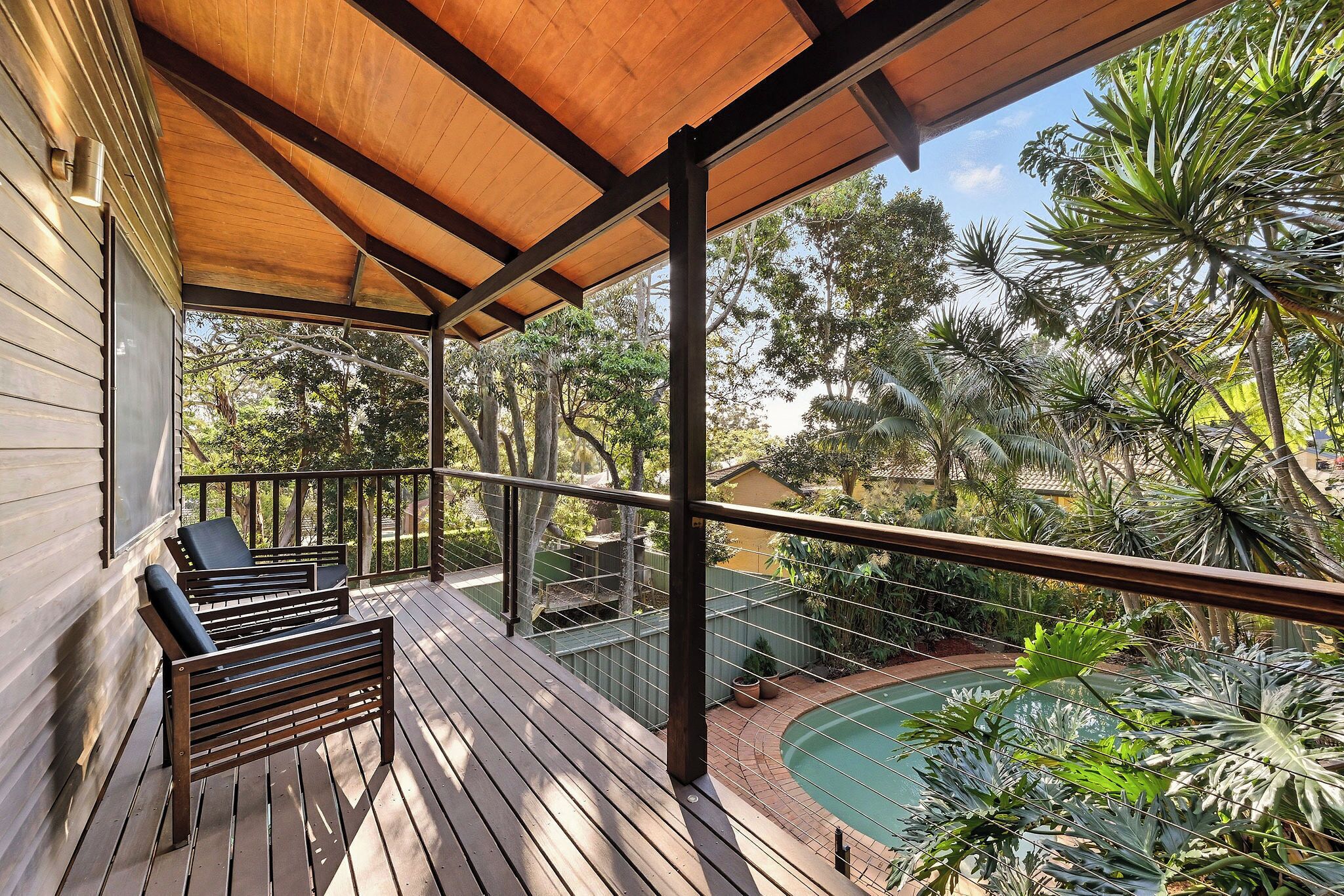Terraza de madera con piscina y exuberante vegetación tropical.